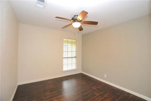 an empty room with wooden floor fan and windows