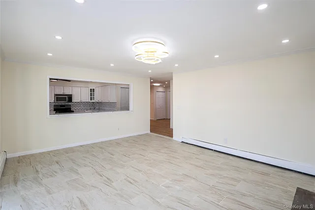an empty room with wooden floor and kitchen view