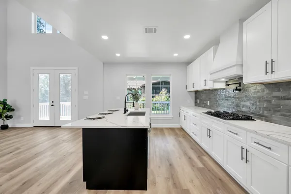 a kitchen with stainless steel appliances granite countertop a sink dishwasher a stove and white cabinets with wooden floor