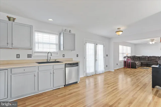 a large white kitchen with stainless steel appliances granite countertop a sink dishwasher stove and white cabinets with wooden floor