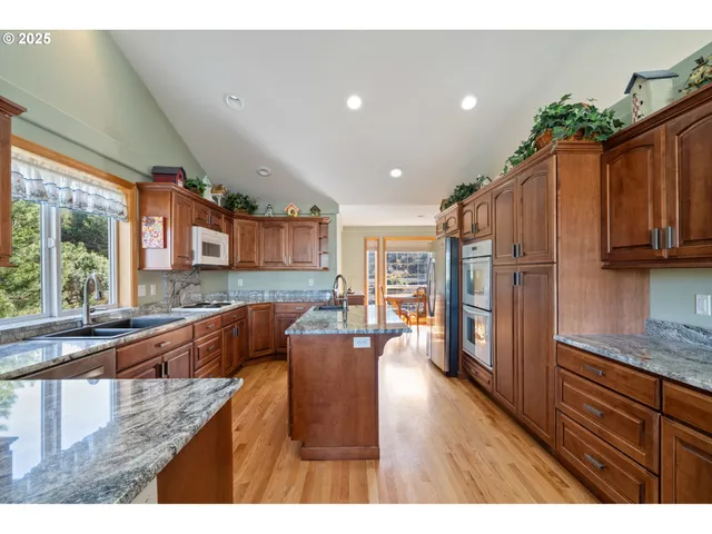 a kitchen with stainless steel appliances granite countertop wooden cabinets a refrigerator a stove a sink and dishwasher with wooden floor