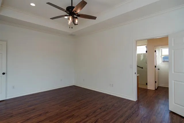 an empty room with wooden floor chandelier fan and windows