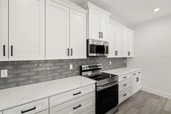 a kitchen with stainless steel appliances a stove a sink a refrigerator and white cabinets with wooden floor