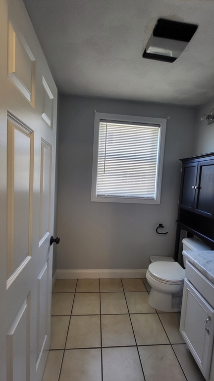 129 Manchester Street, Unit B Lowell, MA 01852 - Photo 9 of 26 a bathroom with a granite countertop toilet a sink a mirror and a window