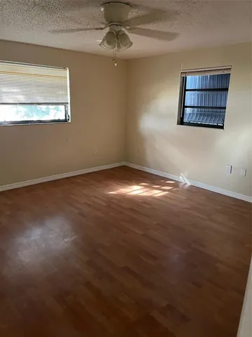 an empty room with wooden floor chandelier fan and windows