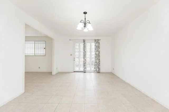 an empty room with chandelier fan and windows