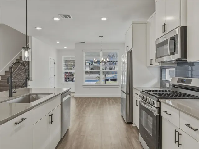 a kitchen with stainless steel appliances a refrigerator a stove a sink cabinets and wooden floor