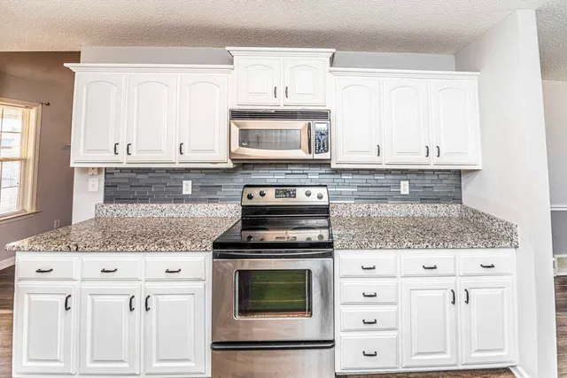 a kitchen with granite countertop white cabinets and stainless steel appliances