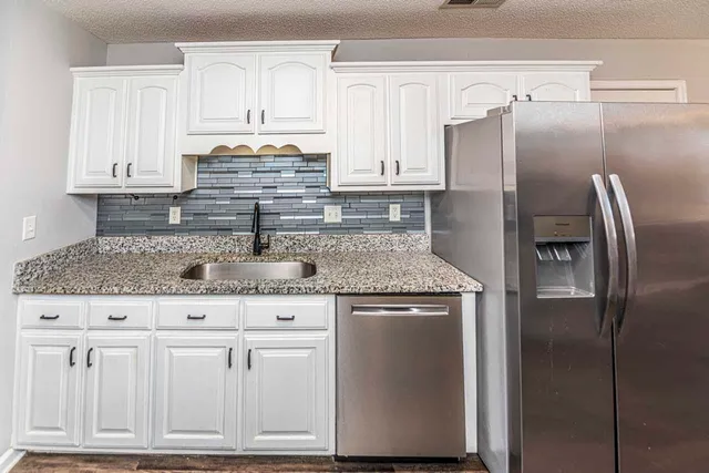 a kitchen with granite countertop a refrigerator sink and cabinets