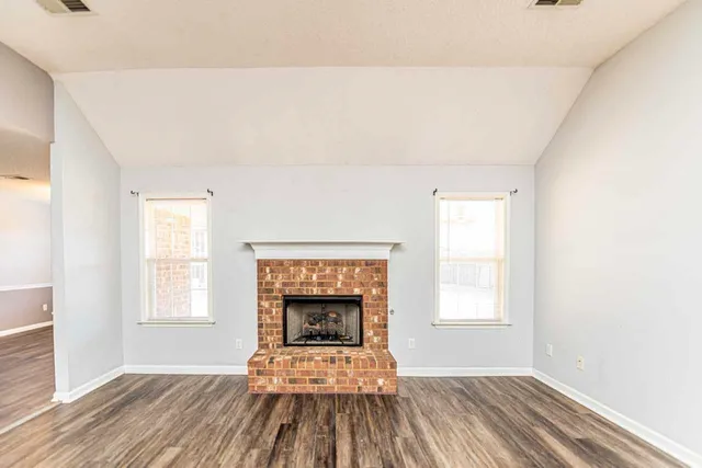 a view of an empty room with wooden floor fireplace and a window