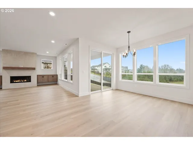 a view of an empty room with wooden floor kitchen view and a window