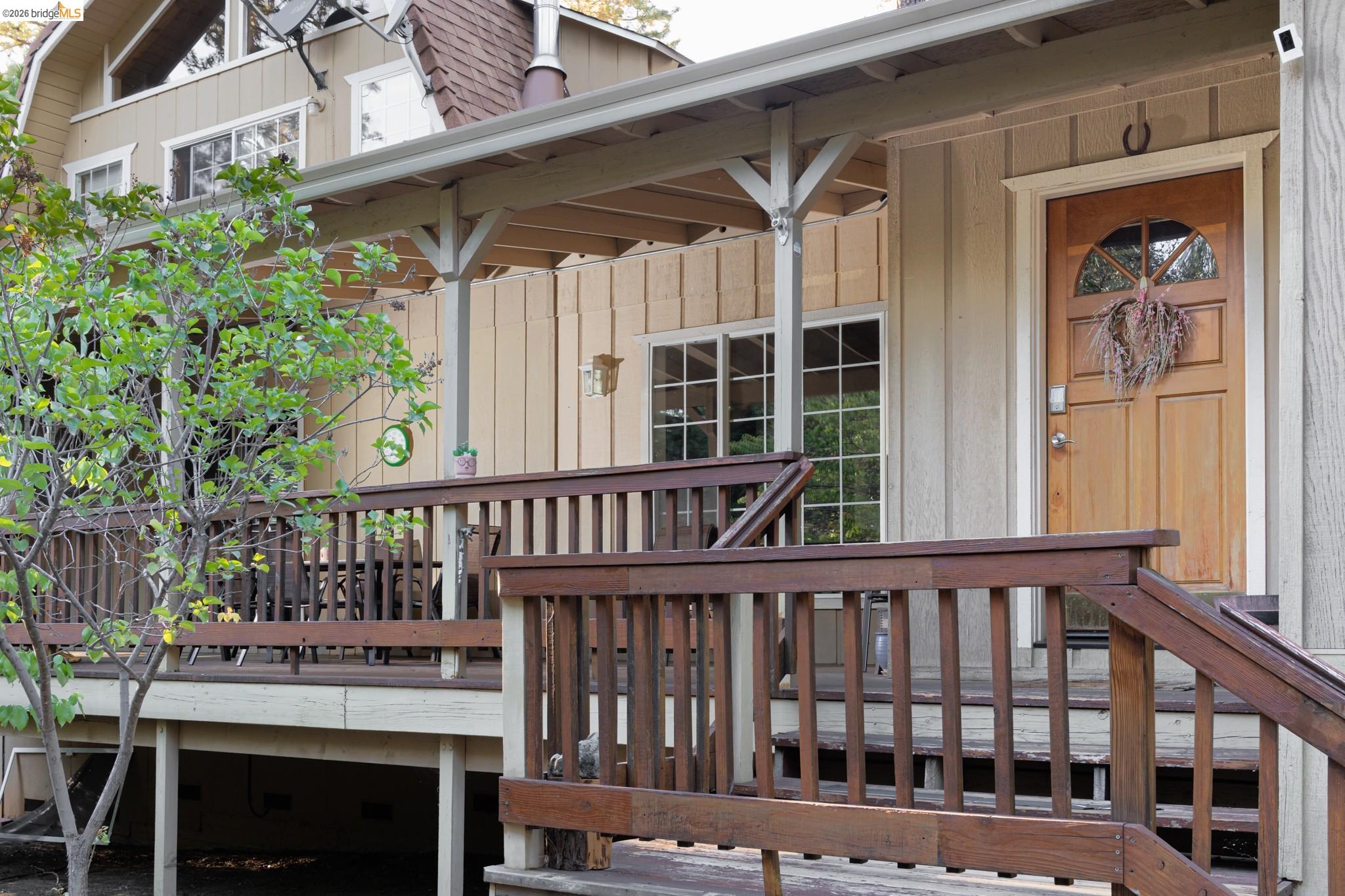 Expansive wooden deck with coordinating railings, covered porch entry, natural wood-finish door with arched glass insert, and multi-pane windows