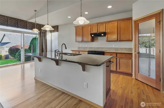 a kitchen with kitchen island granite countertop wooden floors and a view of living room