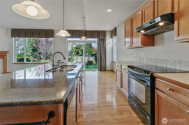 a kitchen with stainless steel appliances granite countertop a sink a stove and a wooden floors