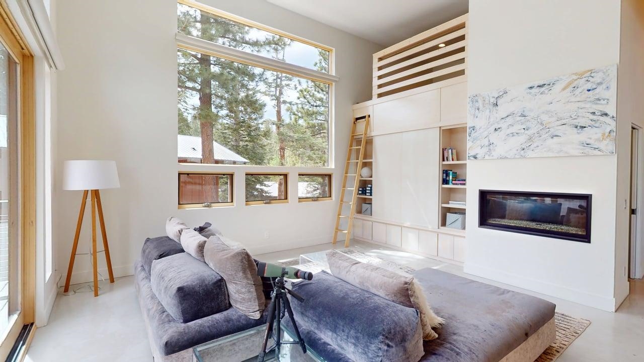 229 Ridgecrest Drive Mammoth Lakes, CA 93546 - Photo 8 of 74 Living area featuring a floor-to-ceiling window, built-in shelving, a ladder accessing an upper space, a linear electric fireplace, and light-toned flooring