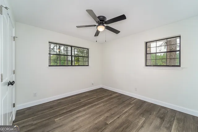 an empty room with wooden floor ceiling fan and windows