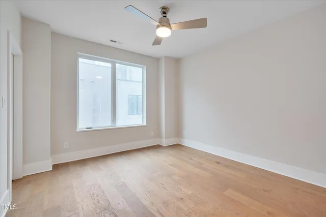 an empty room with wooden floor ceiling fan and windows