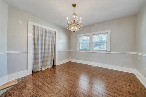 an empty room with wooden floor chandelier and windows