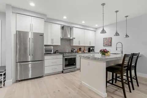 a kitchen with stainless steel appliances white cabinets a sink a stove a refrigerator and island with wooden floor