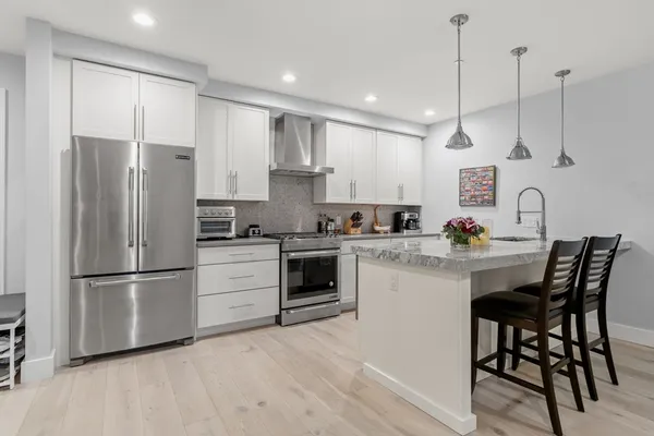a kitchen with stainless steel appliances white cabinets a sink a stove a refrigerator and island with wooden floor