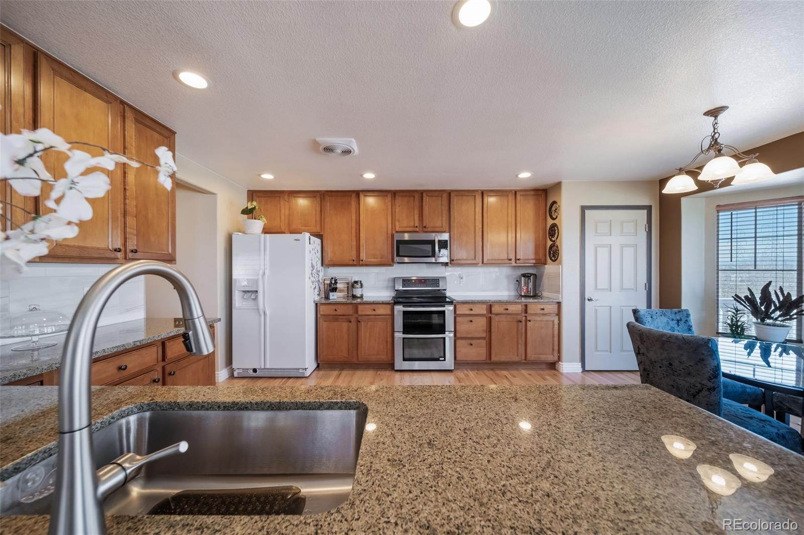 3041 South Jericho Way Aurora, CO 80013 - Photo 13 of 46 a kitchen with stainless steel appliances kitchen island granite countertop a stove a refrigerator a oven a sink with a dining table and chairs