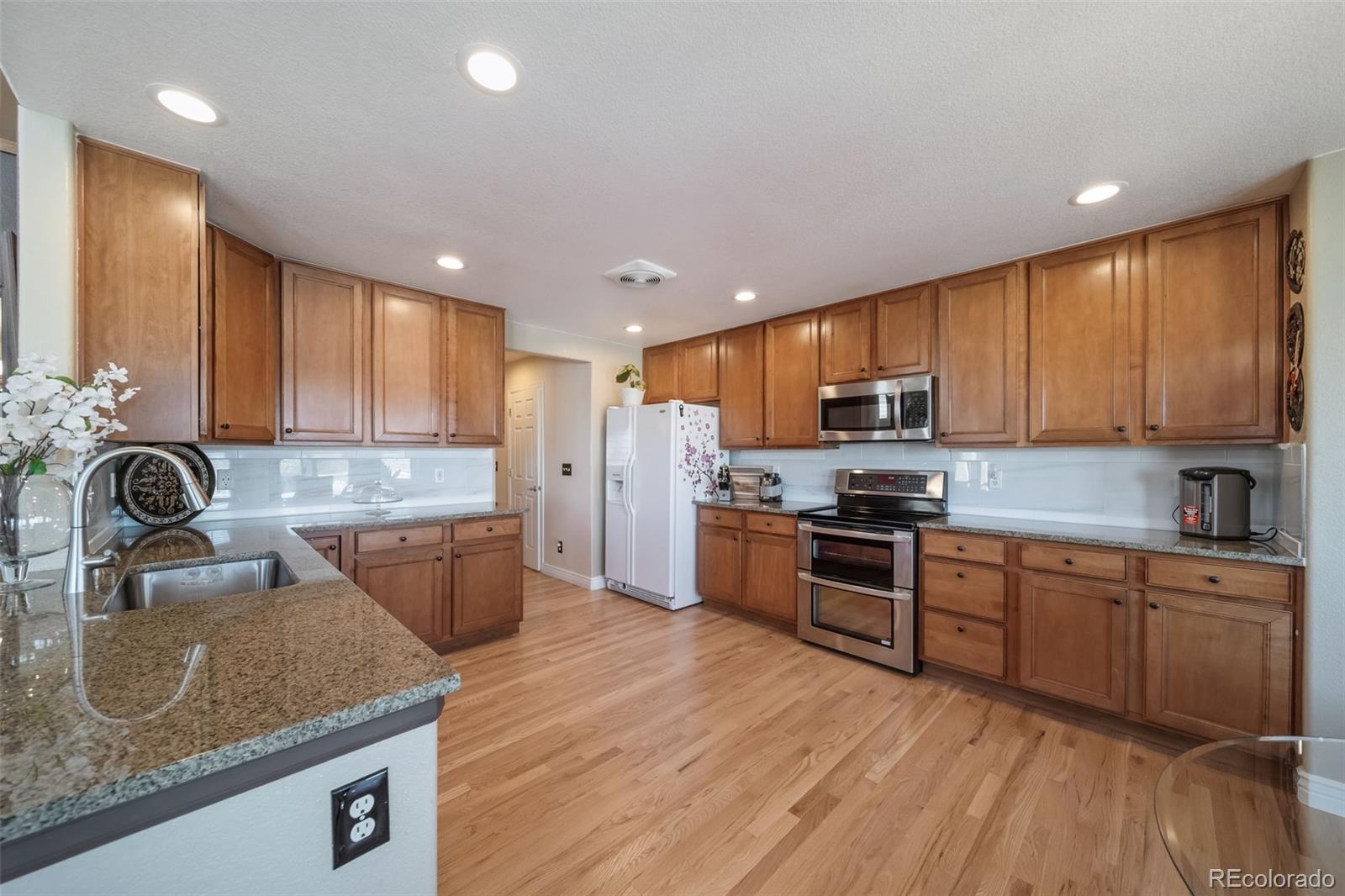 3041 South Jericho Way Aurora, CO 80013 - Photo 14 of 46 a kitchen with stainless steel appliances granite countertop wooden cabinets a sink dishwasher a stove and a refrigerator with wooden floor