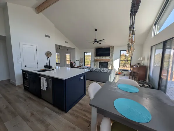 a living room with stainless steel appliances kitchen island granite countertop a table chairs and a wooden floor