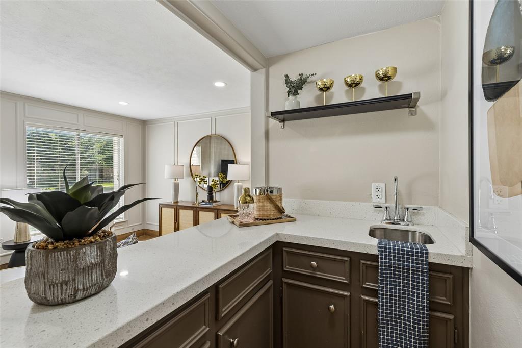 4962 Thunder Road Dallas, TX 75244 - Photo 11 of 26 Wet bar featuring a stainless steel sink, quartz-finish countertop, dark wood-finish cabinetry, and an open display shelf