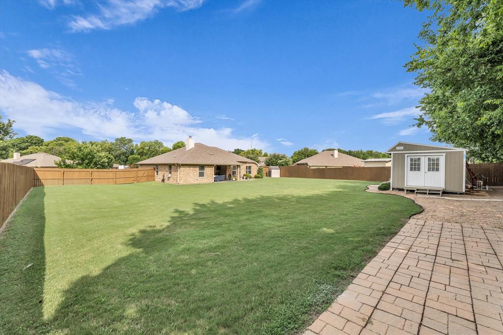 910 Springdale Lane Lorena, TX 76655 - Photo 34 of 39 Expansive backyard featuring a manicured lawn, full privacy fencing, a paved patio area, and a detached storage shed with double doors