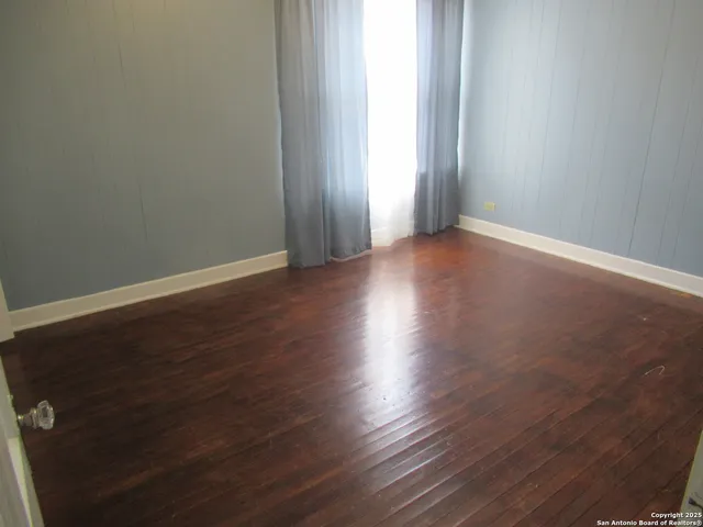 an empty room with wooden floor and windows with curtains