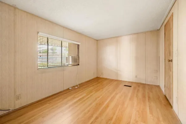 a view of an empty room with wooden floor and a window