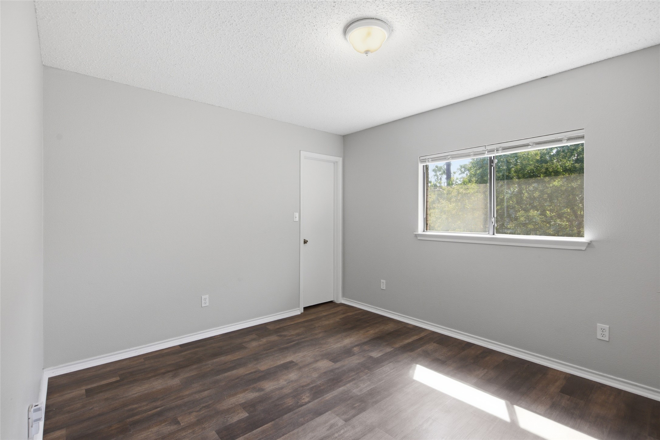 7900 Rosenberry Drive Austin, TX 78747 - Photo 15 of 27 A well-lit bedroom featuring durable plank flooring and a window overlooking lush greenery.