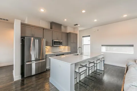 a kitchen with stainless steel appliances granite countertop a refrigerator a stove a sink a dining table and chairs with wooden floor