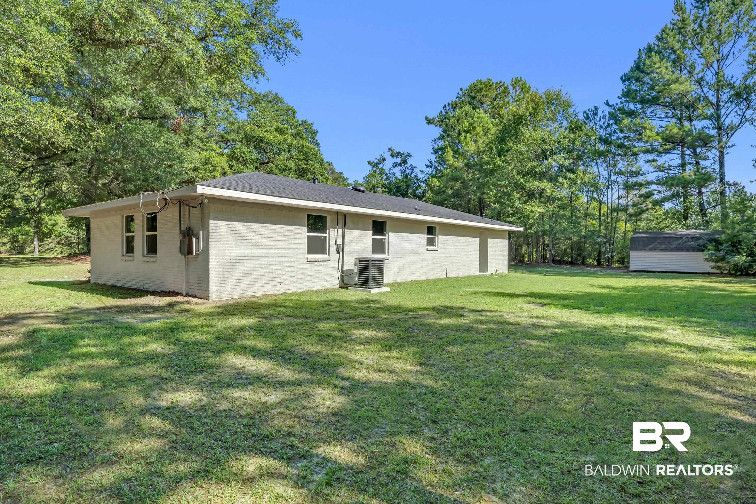 2712 Shelton Beach Rd Extension Mobile, AL 36613 - Photo 22 of 24 Expansive green lawn surrounds this property featuring a light-colored brick exterior, dark shingle roof, multiple windows, and mature trees providing natural screening