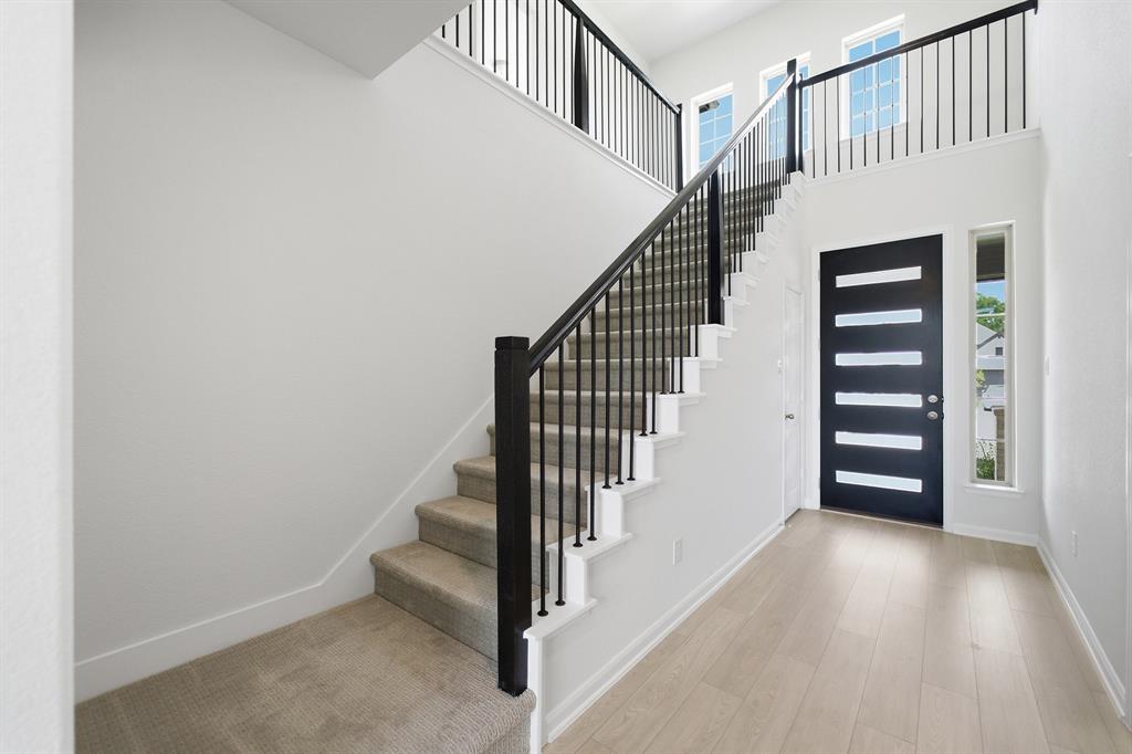1908 Sangallo Lane Celina, TX 75009 - Photo 35 of 35 Bright entryway featuring a modern black door with horizontal glass insets, light wood-finish flooring, and a contemporary staircase with black metal balusters and carpeted treads