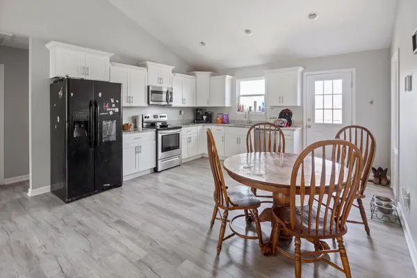 a kitchen with stainless steel appliances granite countertop a dining table chairs refrigerator and window