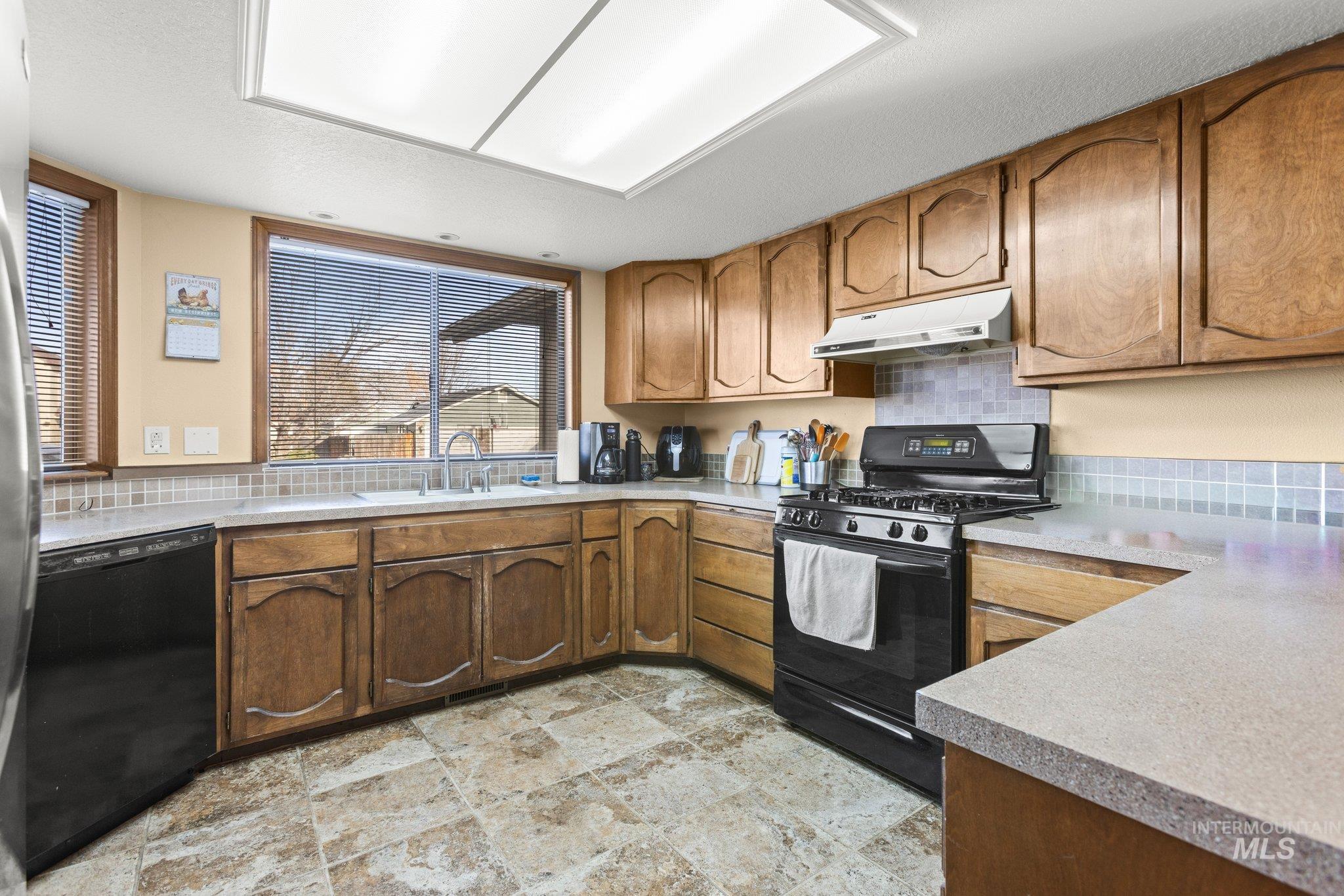 7567 Sundance Drive Boise, ID 83709 - Photo 11 of 21 Kitchen with black appliances, decorative backsplash, stone finish floors, wood finish cabinets, and a textured ceiling