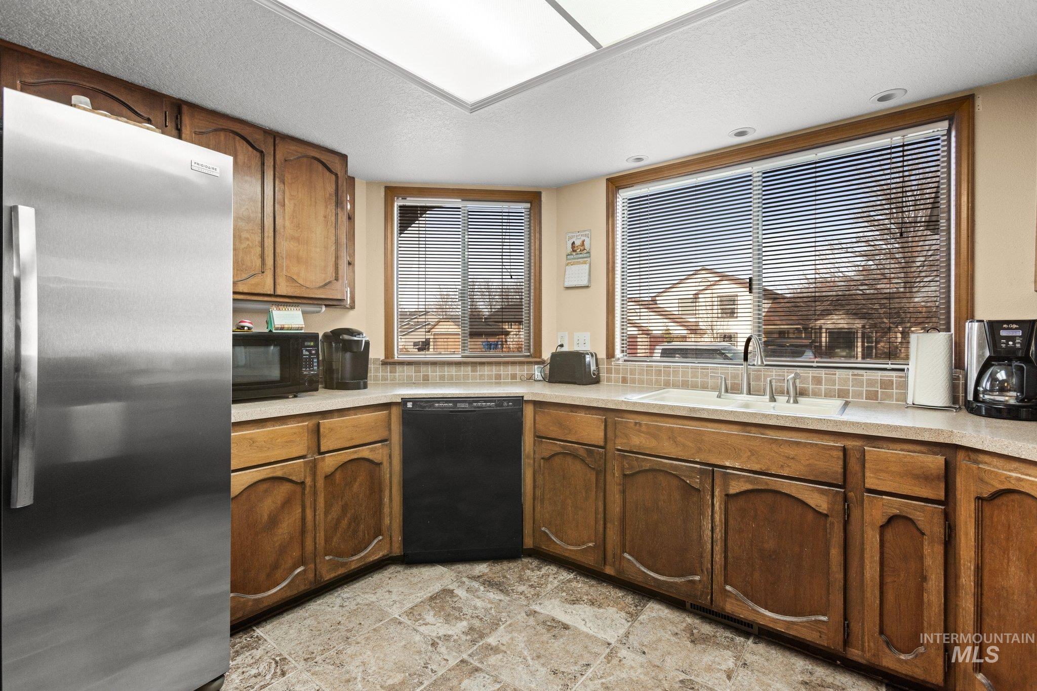 7567 Sundance Drive Boise, ID 83709 - Photo 12 of 21 Kitchen with black appliances, light countertops, a textured ceiling, wood finish cabinets, and stone finish floors
