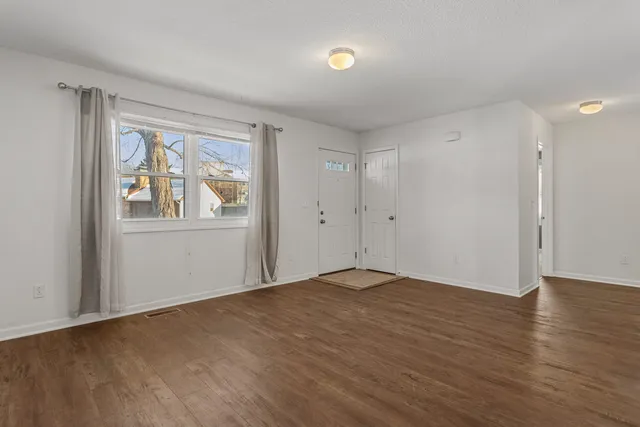 a view of an empty room with wooden floor and windows