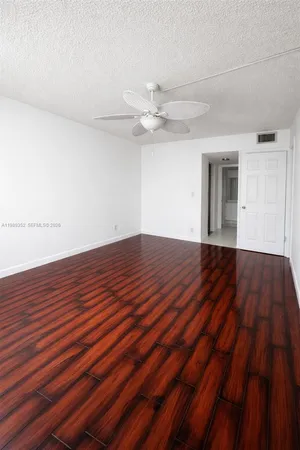 a view of an empty room with wooden floor and a ceiling fan