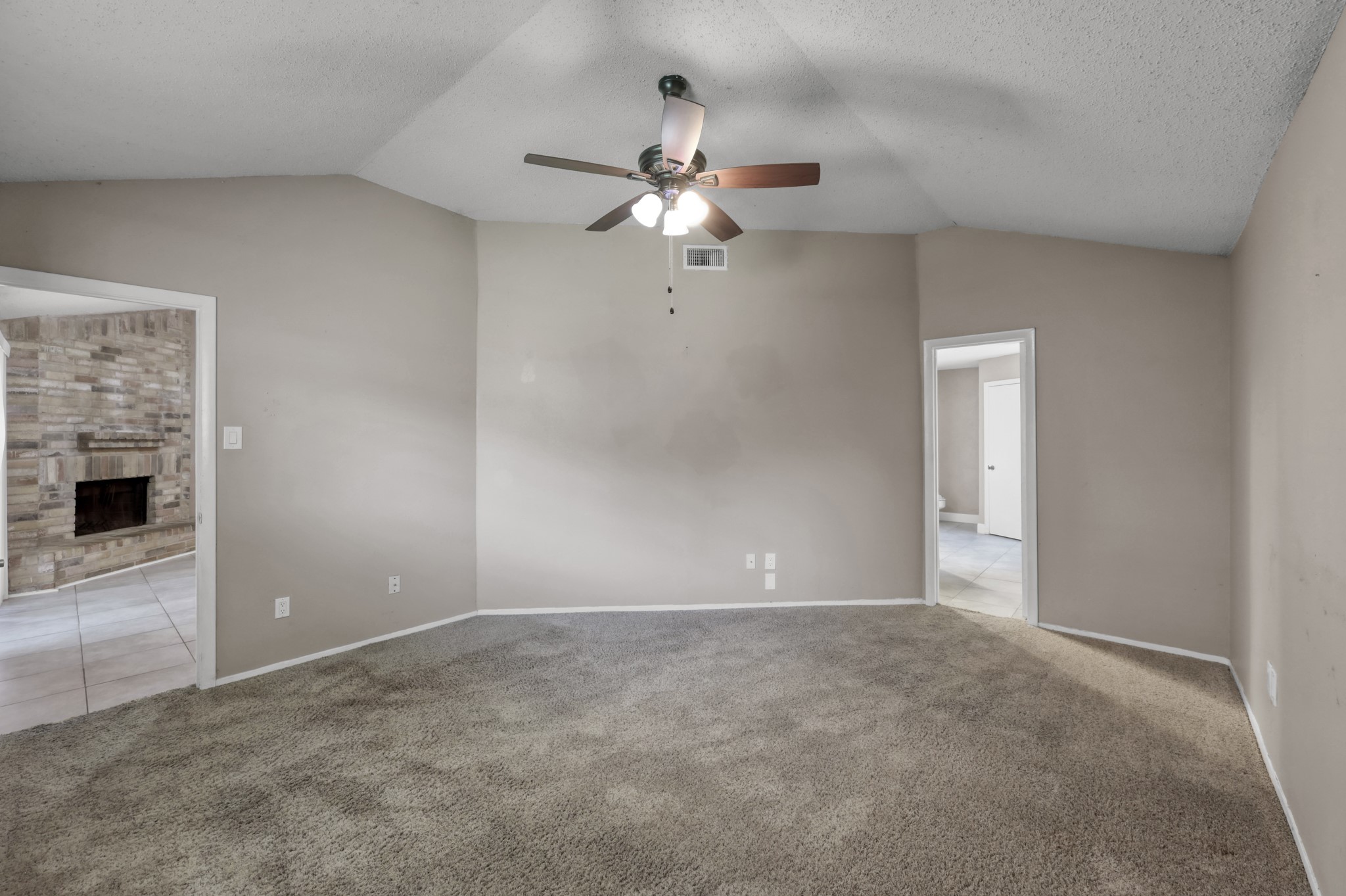12015 Fallbrook Drive Houston, TX 77065 - Photo 16 of 29 This room features neutral walls, carpeted flooring, and a ceiling fan. It connects to a tiled area with a stone fireplace, providing a cozy and versatile space.
