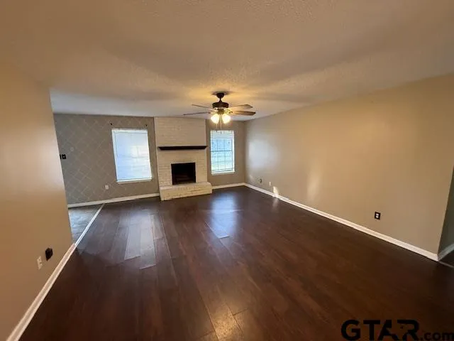 an empty room with wooden floor fireplace and windows