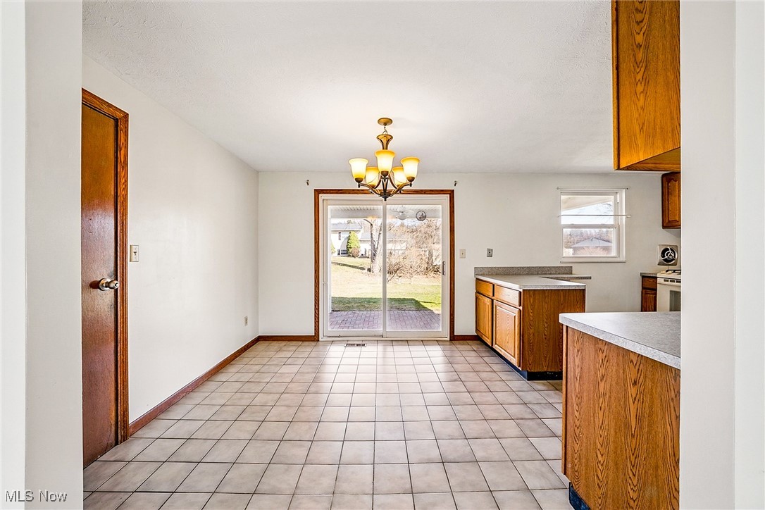 803 Renninger Road Akron, OH 44319 - Photo 8 of 44 Kitchen featuring baseboards, light countertops, brown cabinets, light tile patterned flooring, and a notable chandelier