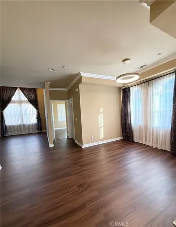 an empty room with wooden floor and windows with curtains
