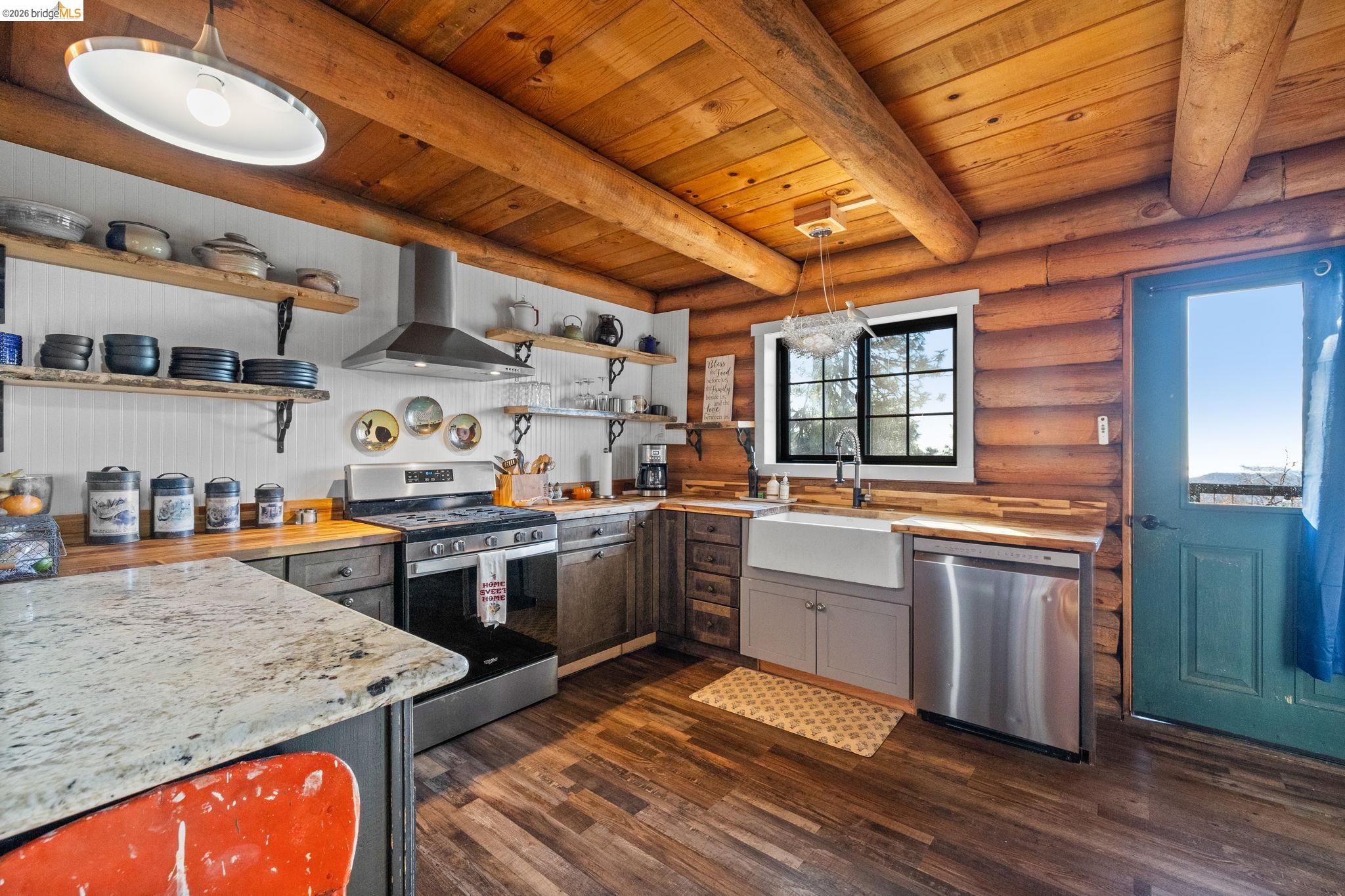 16144 Big Hill Road Sonora, CA 95370 - Photo 16 of 51 Kitchen featuring wood-finish flooring, exposed log beam ceiling, stainless steel appliances, a farmhouse sink, and a contrasting light-colored countertop