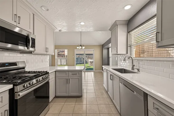 a kitchen with stainless steel appliances granite countertop a sink a stove top oven a refrigerator cabinets and a window