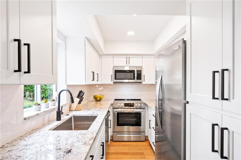 1275 7th Avenue North, Unit 201 Naples, FL 34102 - Photo 12 of 39 Kitchen with stainless steel appliances, white cabinets, light stone countertops, backsplash, and light wood-style floors