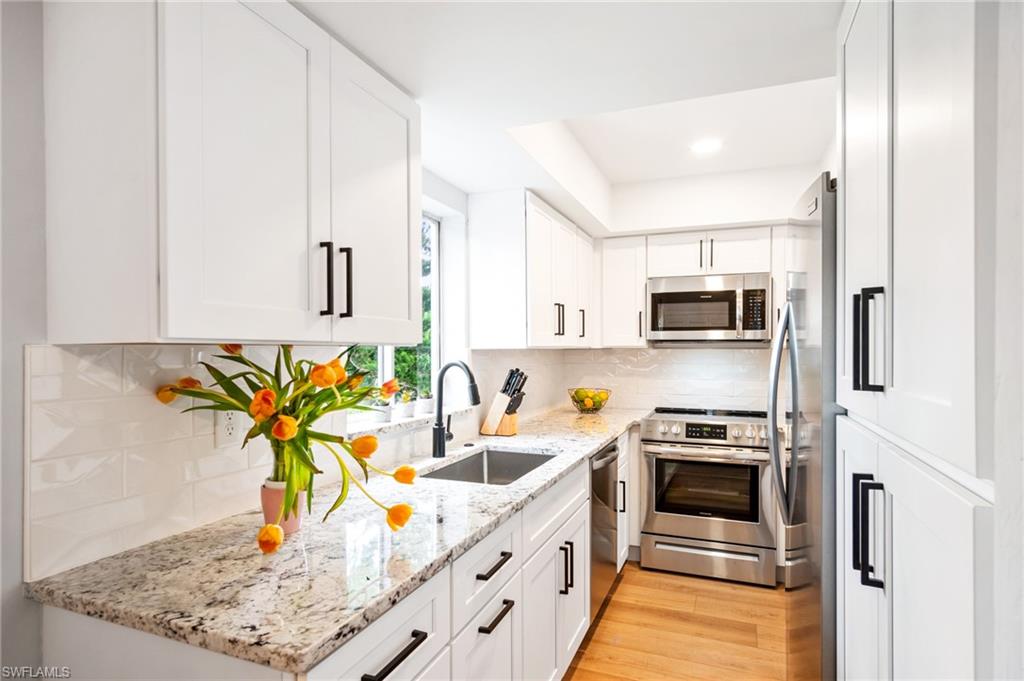 1275 7th Avenue North, Unit 201 Naples, FL 34102 - Photo 5 of 39 Kitchen featuring appliances with stainless steel finishes, white cabinets, light wood finished floors, backsplash, and recessed lighting
