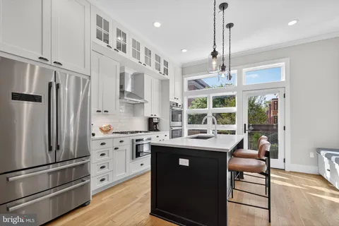 a kitchen with stainless steel appliances kitchen island granite countertop a refrigerator a oven and white cabinets with wooden floors