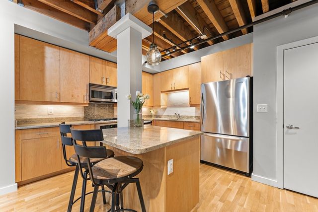 a kitchen with stainless steel appliances granite countertop a refrigerator a sink dishwasher a dining table and chairs with wooden floor